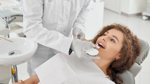 woman-smiling-while-male-dentist-keeping-teeth-color-range-min